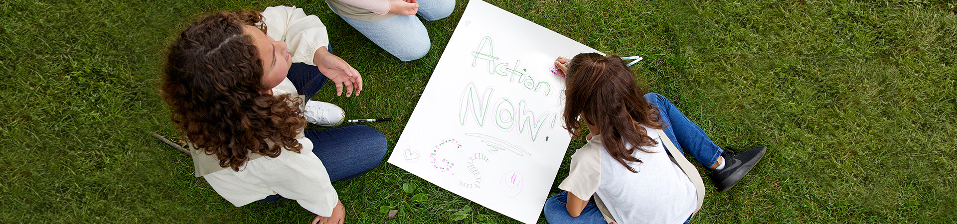  Overhead shot of three girls decorating a poster which reads "Action Now" 