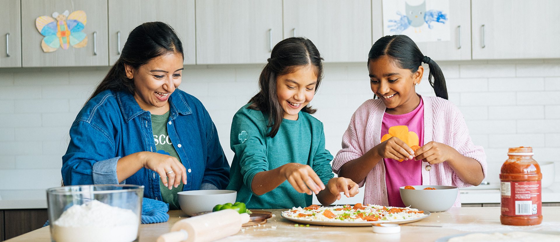 A volunteer and two Girl Scouts making pizza