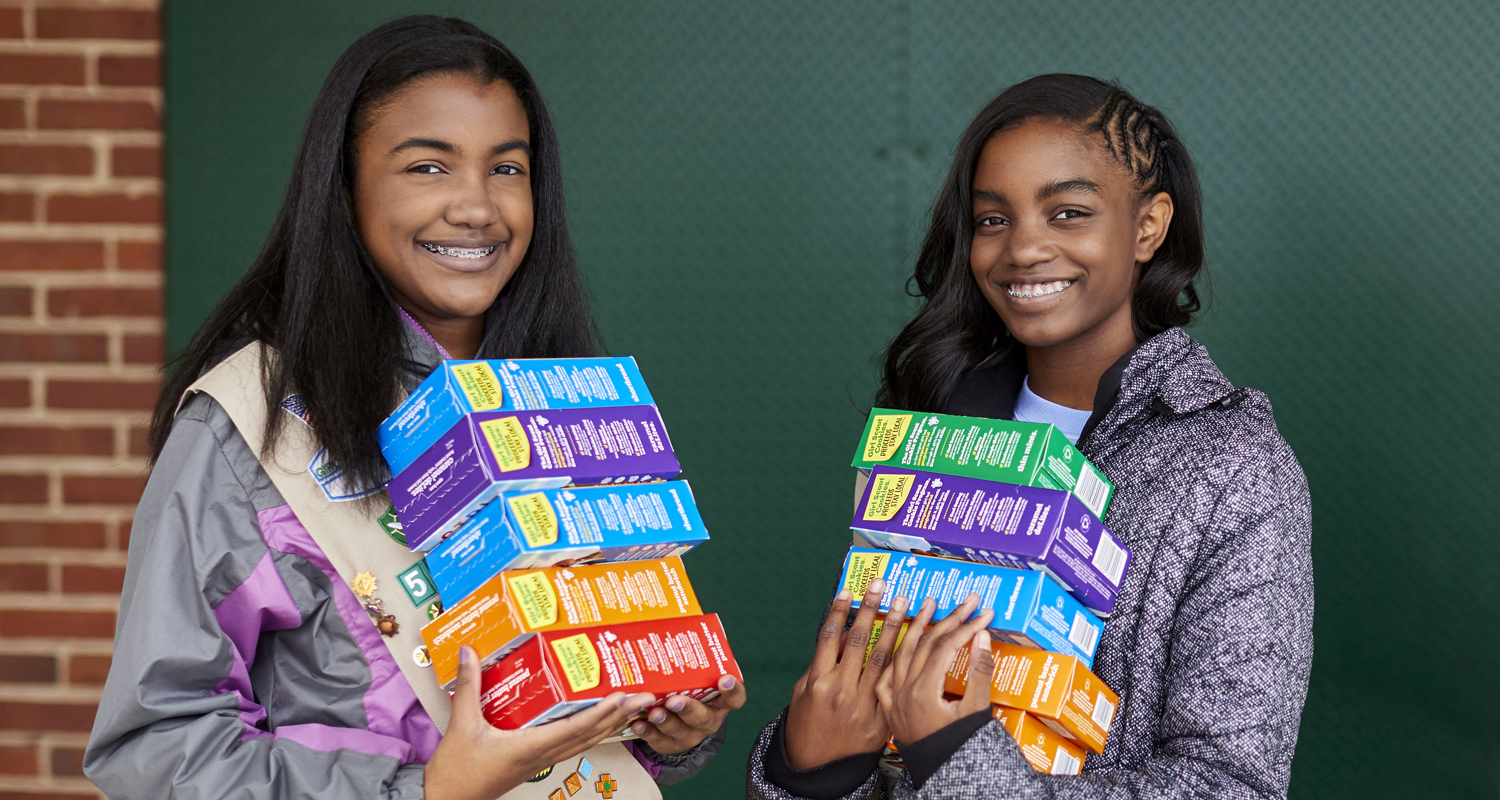  Smiling girl scouts holding a variety of cookie boxes. 