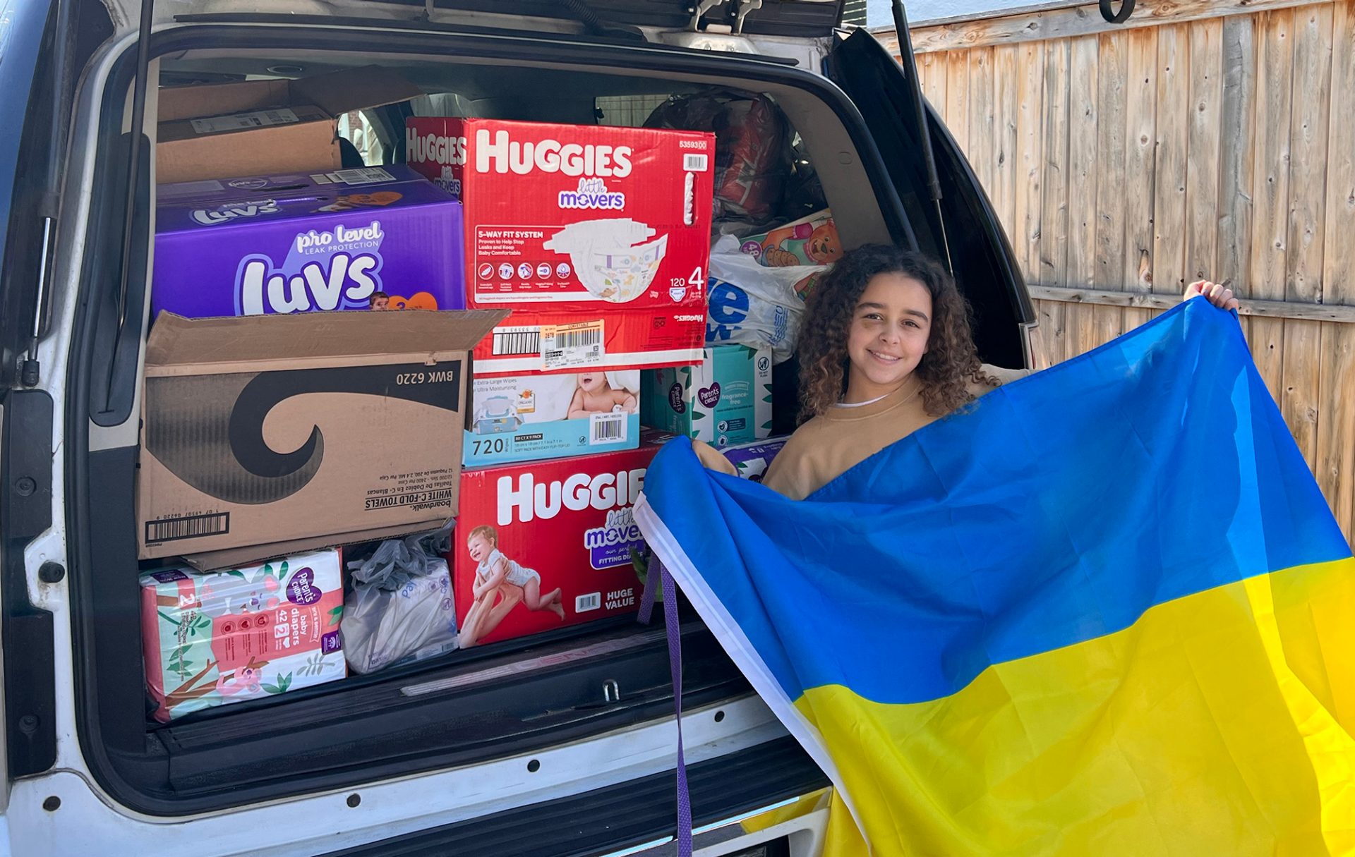 Girl Scout holding a Ukrainian flag in front of a SUV loaded with donations
