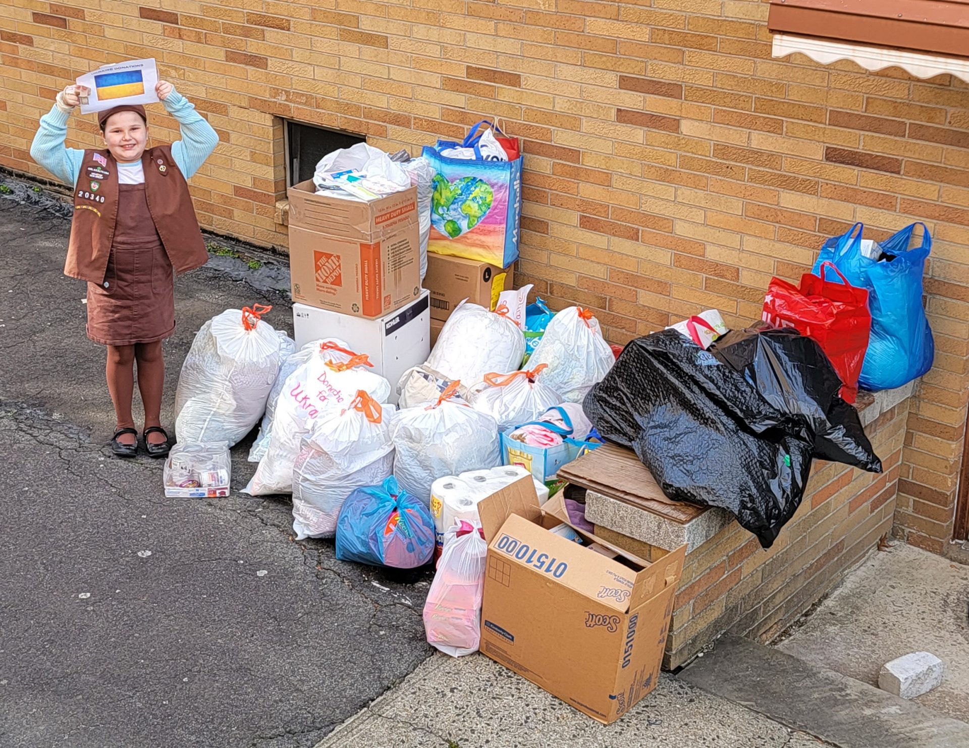 Brownie Girl Scout standing next to a large pile of donations 