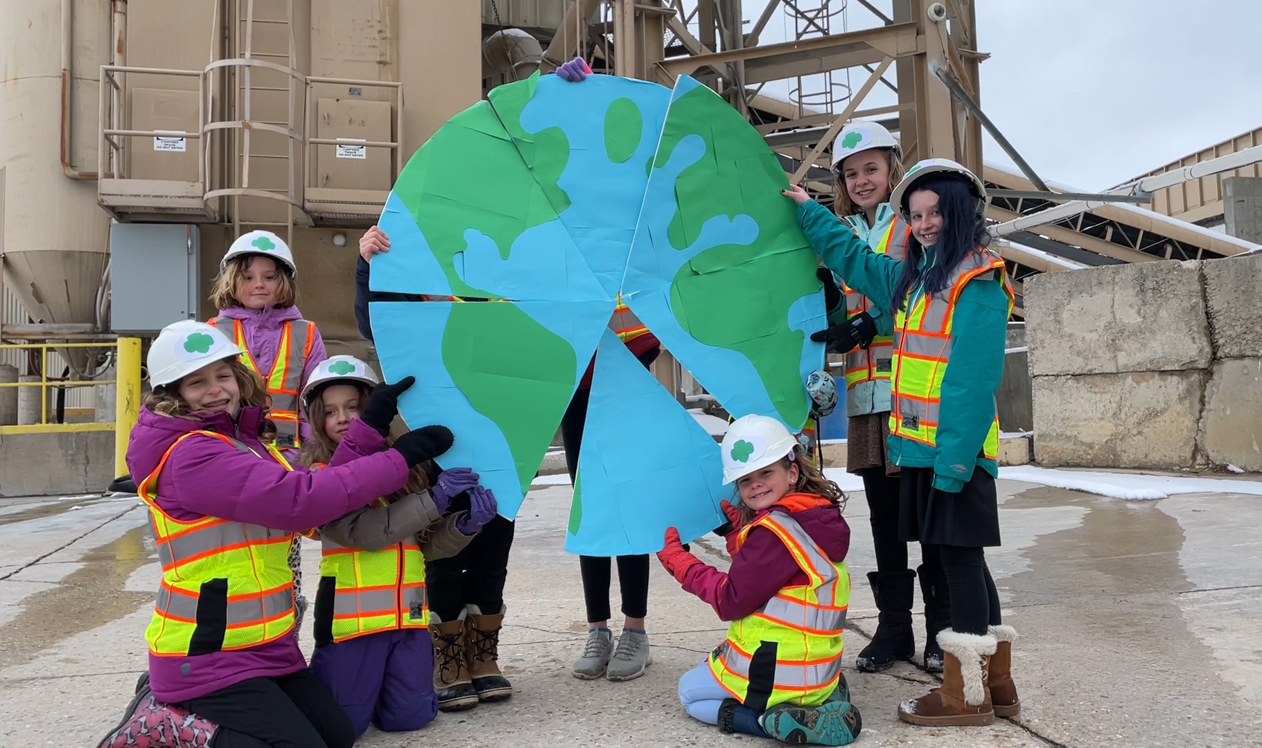girls wearing hardhats holding wedges of a circle together to form a globe