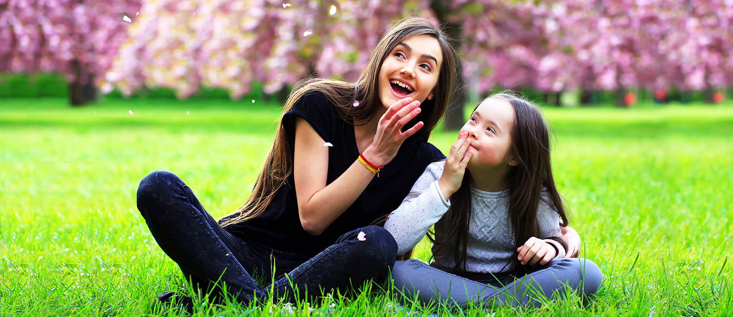  a teen girl sitting, smiling with her sister who has Down's Syndrome 
