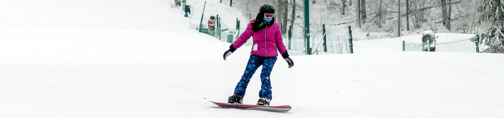  A girl wearing a magenta jacket and blue snow pants snowboarding 