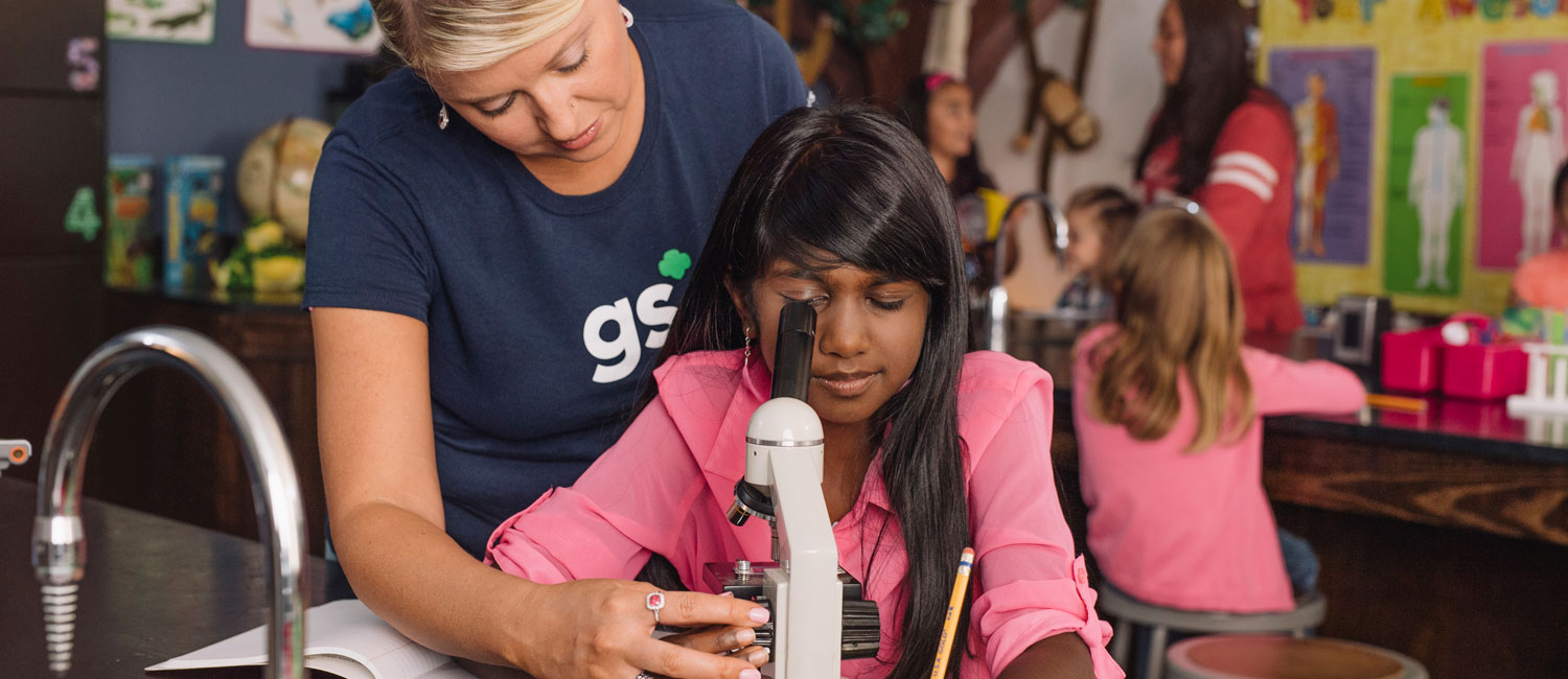  A Junior Girl Scout looking through a microscope, assisted by her troop leader 