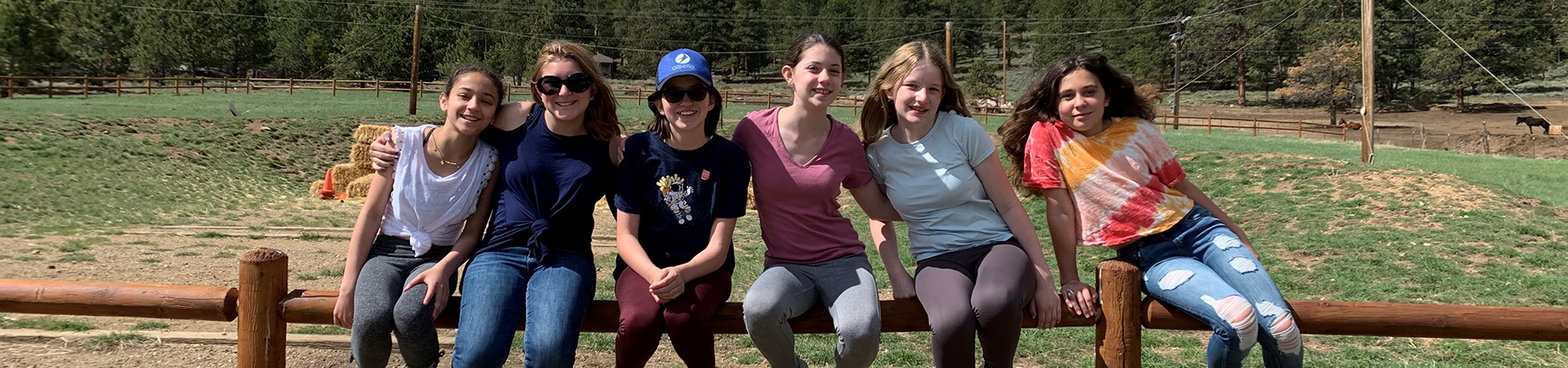  A group of Cadette Girl Scouts sitting on a wooden fence in a rural area 