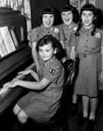 Photo of Girl Scouts gathered around a piano. ©GSUSA. All rights reserved.