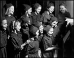 Photo of Girl Scouts singing at a piano. © GSUSA. All rights reserved.
