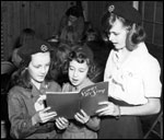 Photo of three girl Scouts singing from a songbook. © GSUSA. All rights reserved.