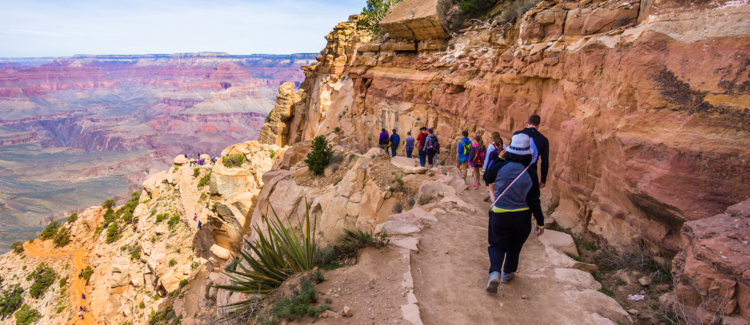 group of girls and women walking on a rocky ledge over a canyon