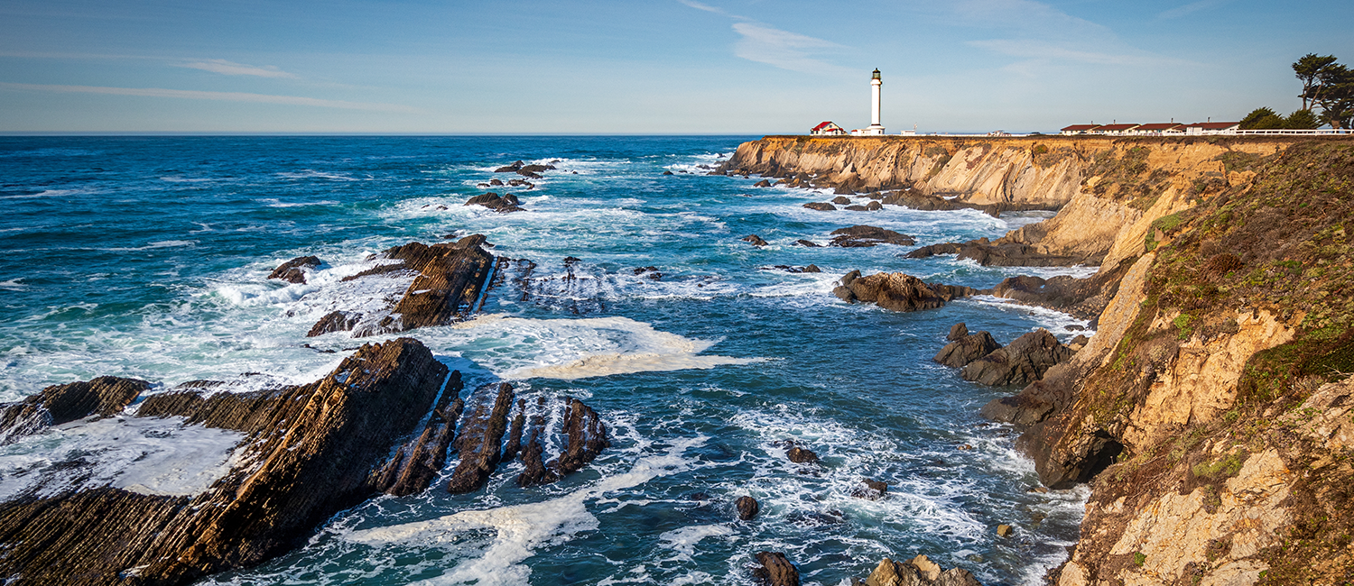 a rocky ocean coastline with a lighthouse in the distance 