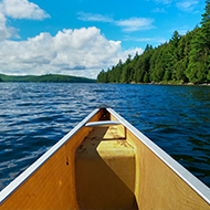 the front of a canoe heading into blue water with trees on both sides
