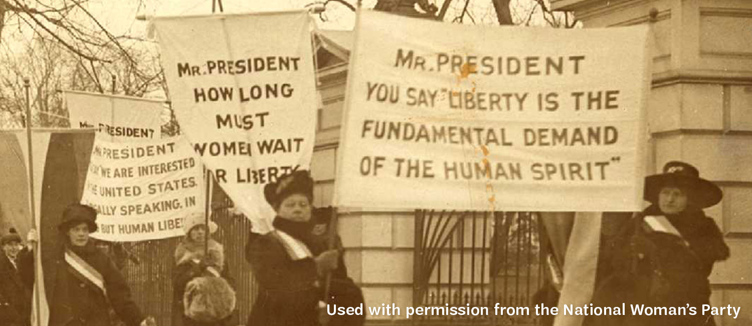 A vintage picture of women advocating for suffrage, holding signs addressing the President