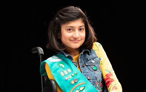 Junior wheelchair user Girl Scout wearing sash and badges similing at camera.