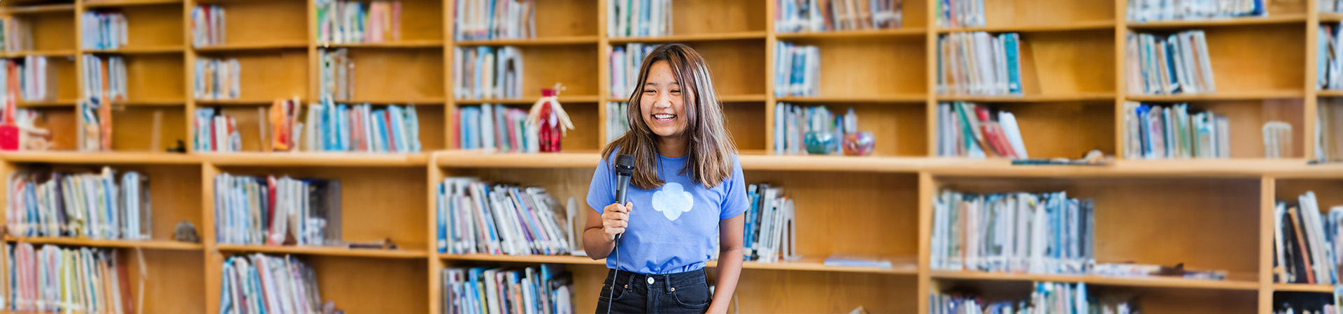  A Girl Scout Senior standing in a library holding a microphone 