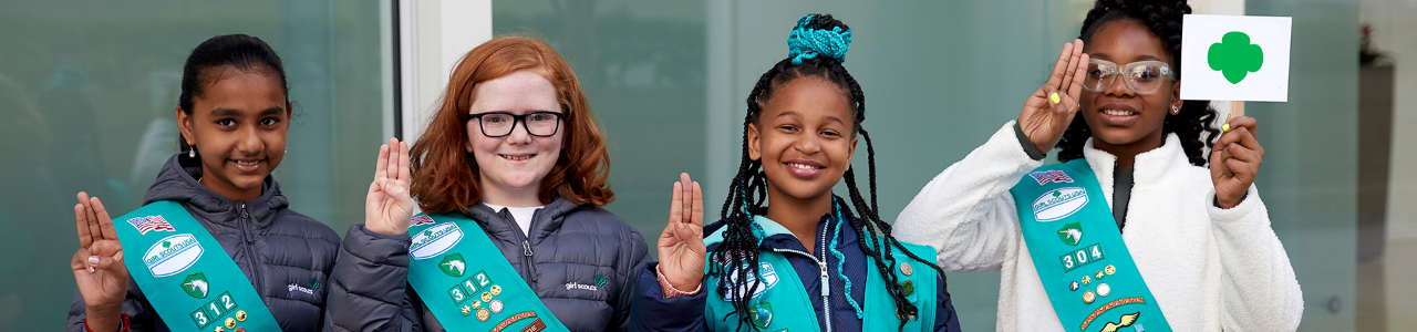  A troop of Junior Girl Scouts holding up the Girl Scout promise sign (three fingers on the right hand, with the thumb holding down the pinky) 