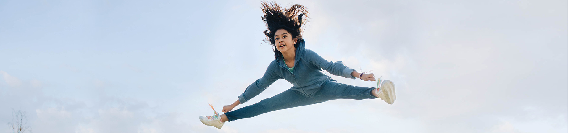  A girl doing a toe touch against a pale blue sky 