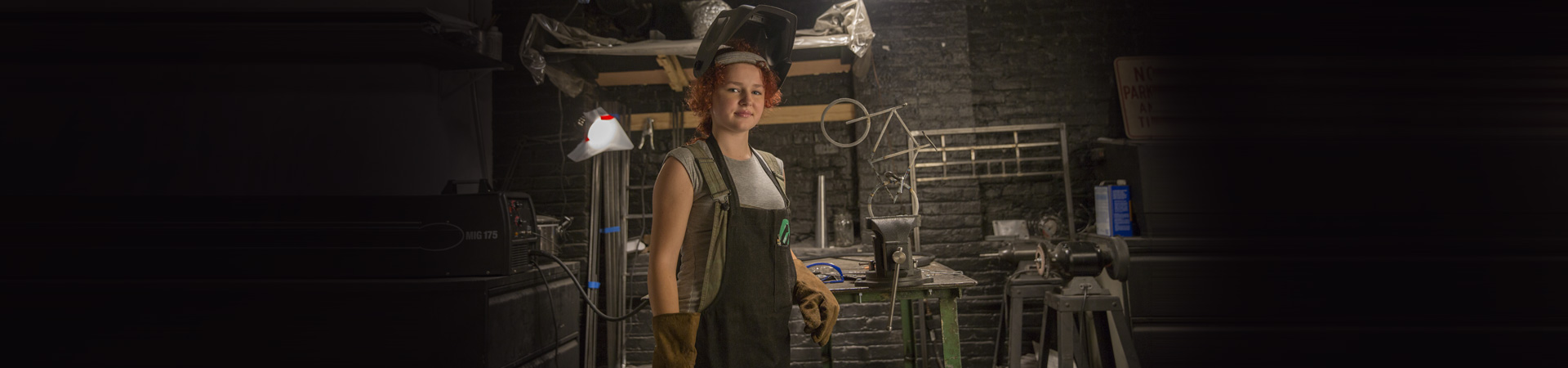  girl wearing welding gear in a metal shop 