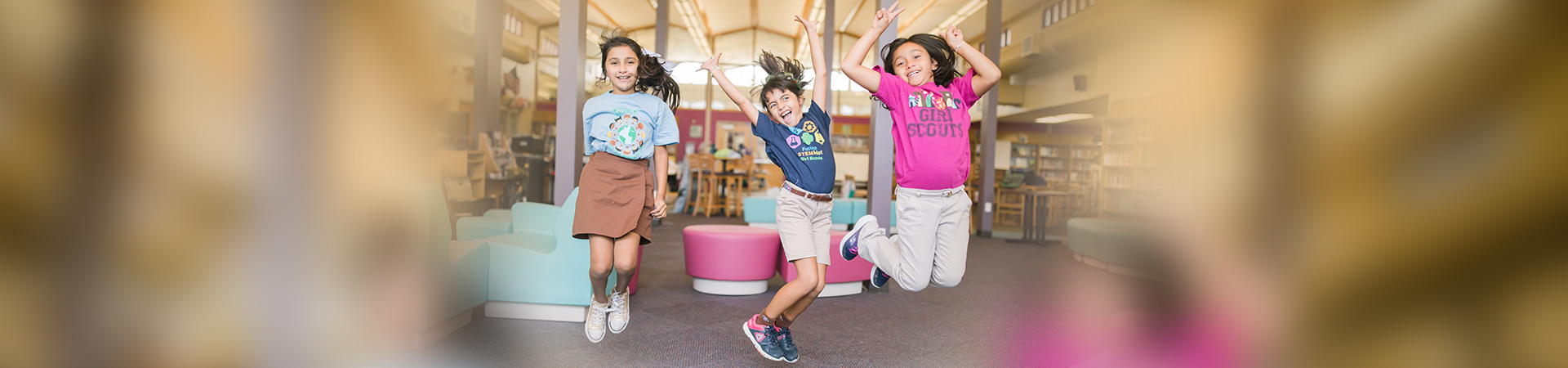 Three Brownie Girl Scouts jumping in a library 