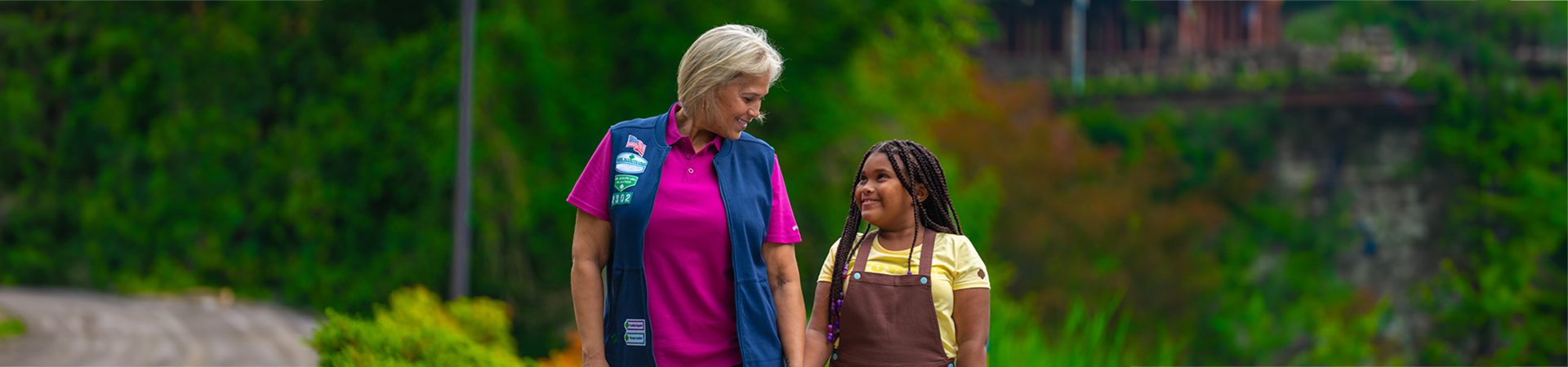  adult woman girl scout volunteer wearing vest outdoors with junior girl scout hiking 