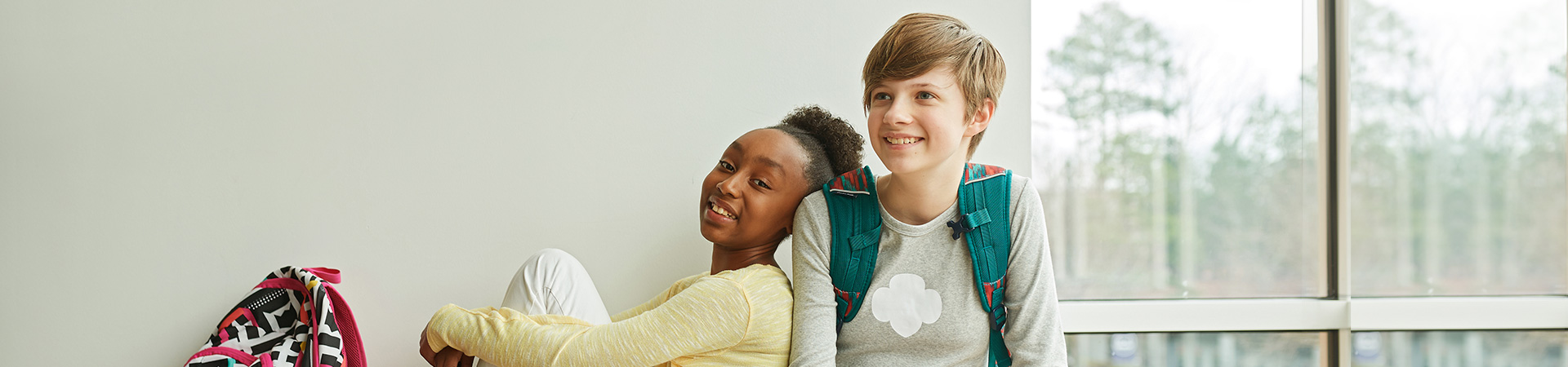  Two middle school Junior Girl Scouts wearing trefoil clothing leaning on one another indoors. 