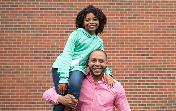 Father with daughter on his shoulder smiling looking at camera.