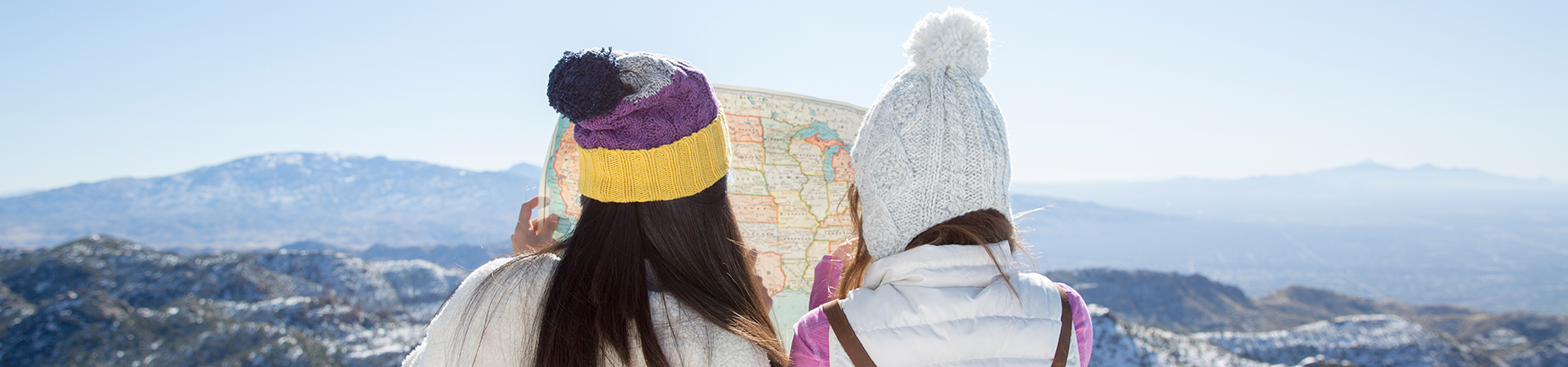  two girls in winter gear standing on a mountain looking at a map 