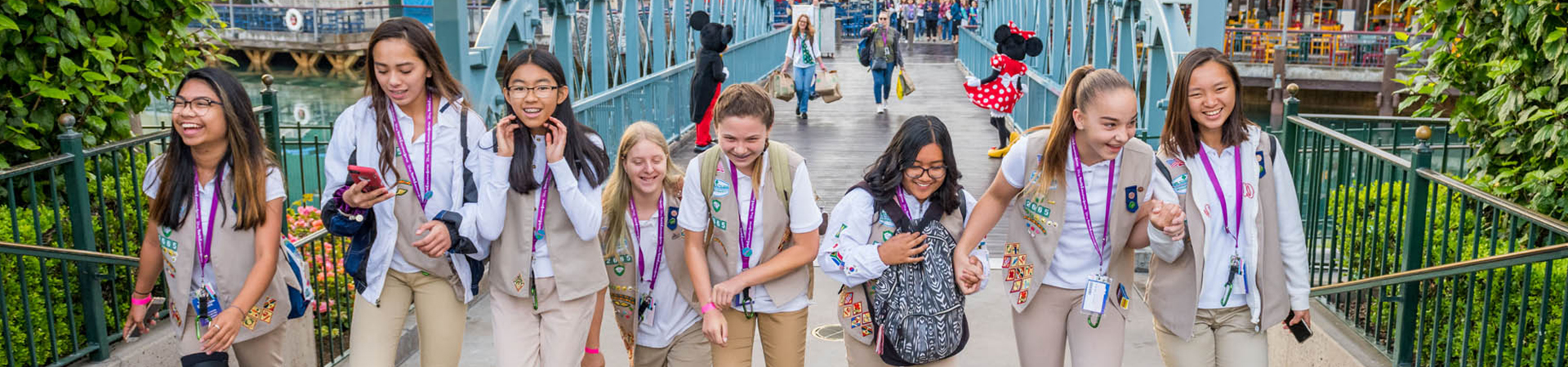  group of cadette girl scouts crossing a bridge with Mickey Mouse and Minnie Mouse in the background 