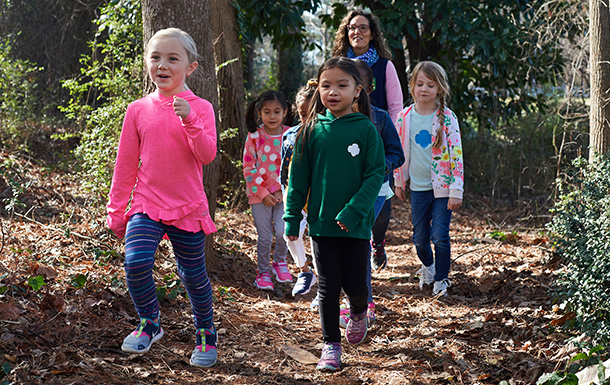 Group of Daisy Girl Scouts hiking outdoors with troop leader