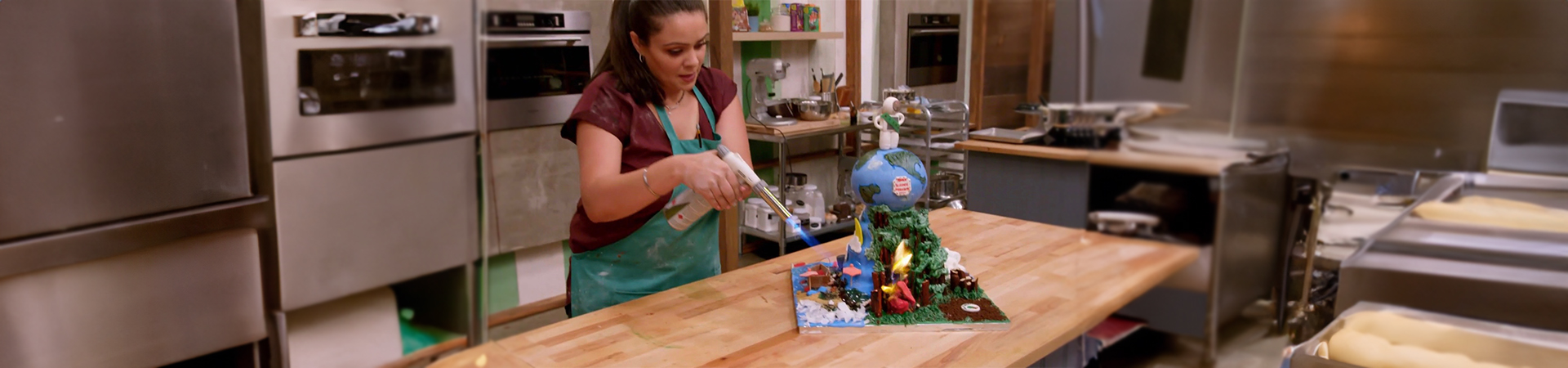  A woman in a professional bakery kitchen using a butane torch on a highly decorated cake 