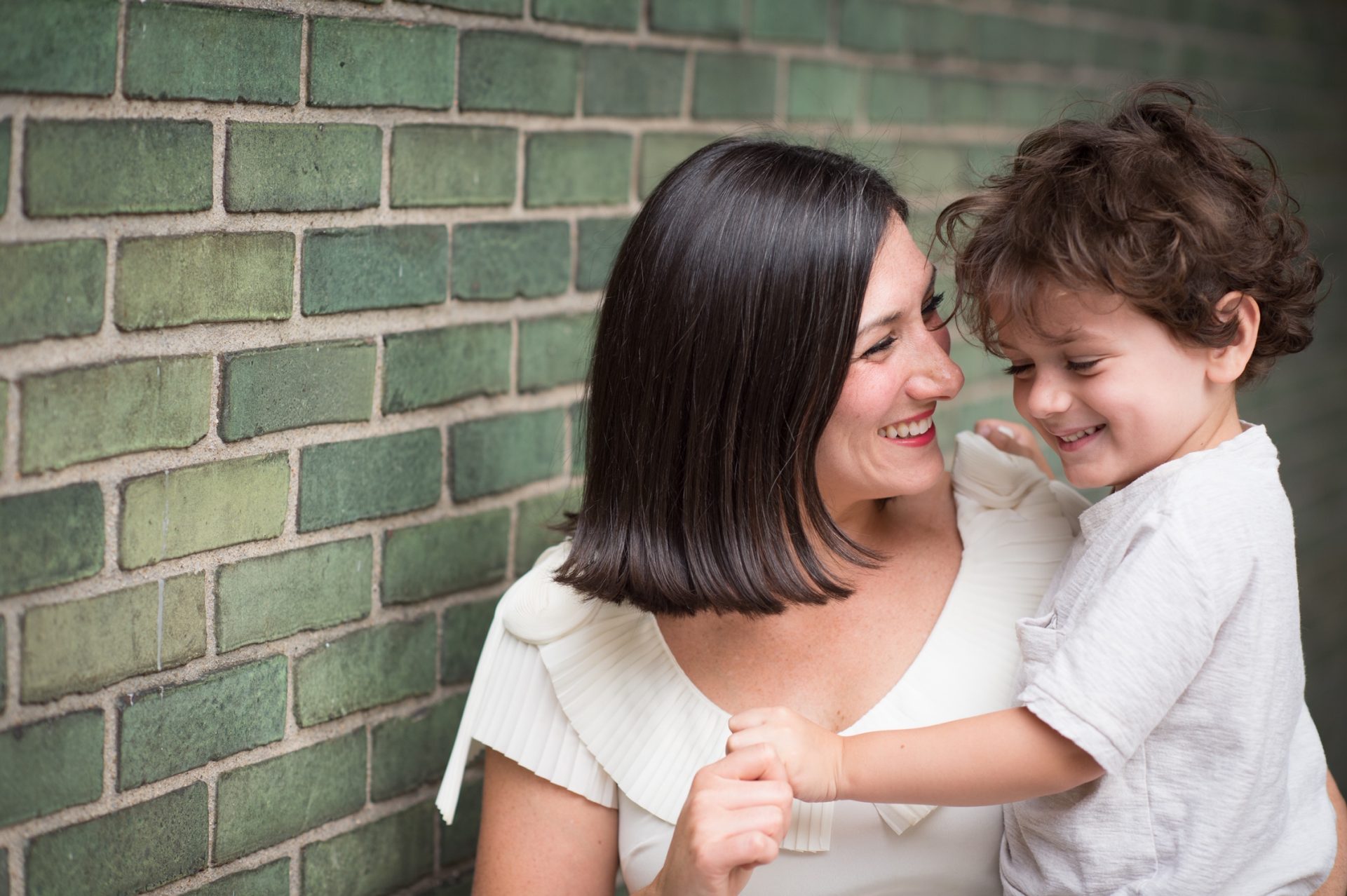  A mother and her young child, wearing white shirts, hugging each other in front of a grey brick wall 