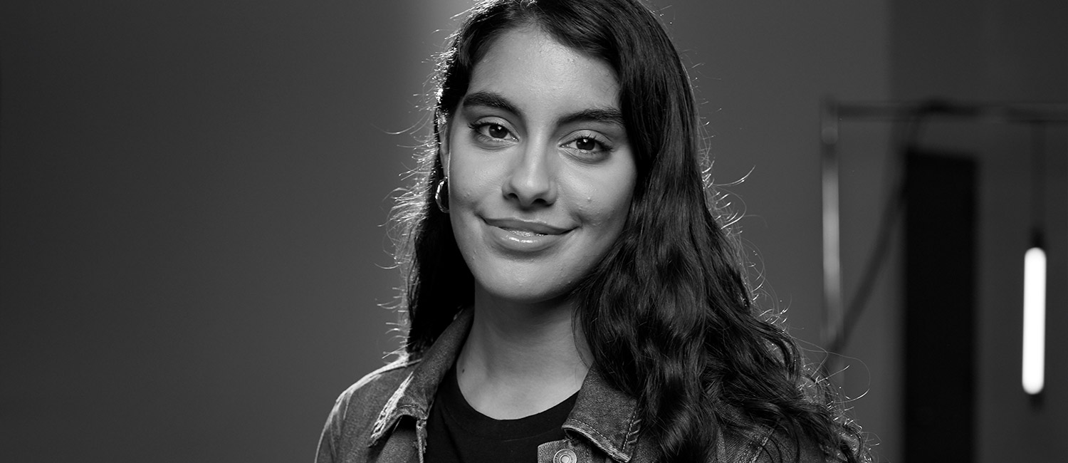  Black and white photo of National Gold Award Girl Scout Ana smiling and wearing hoop earrings, a shirt, and jean jacket. 