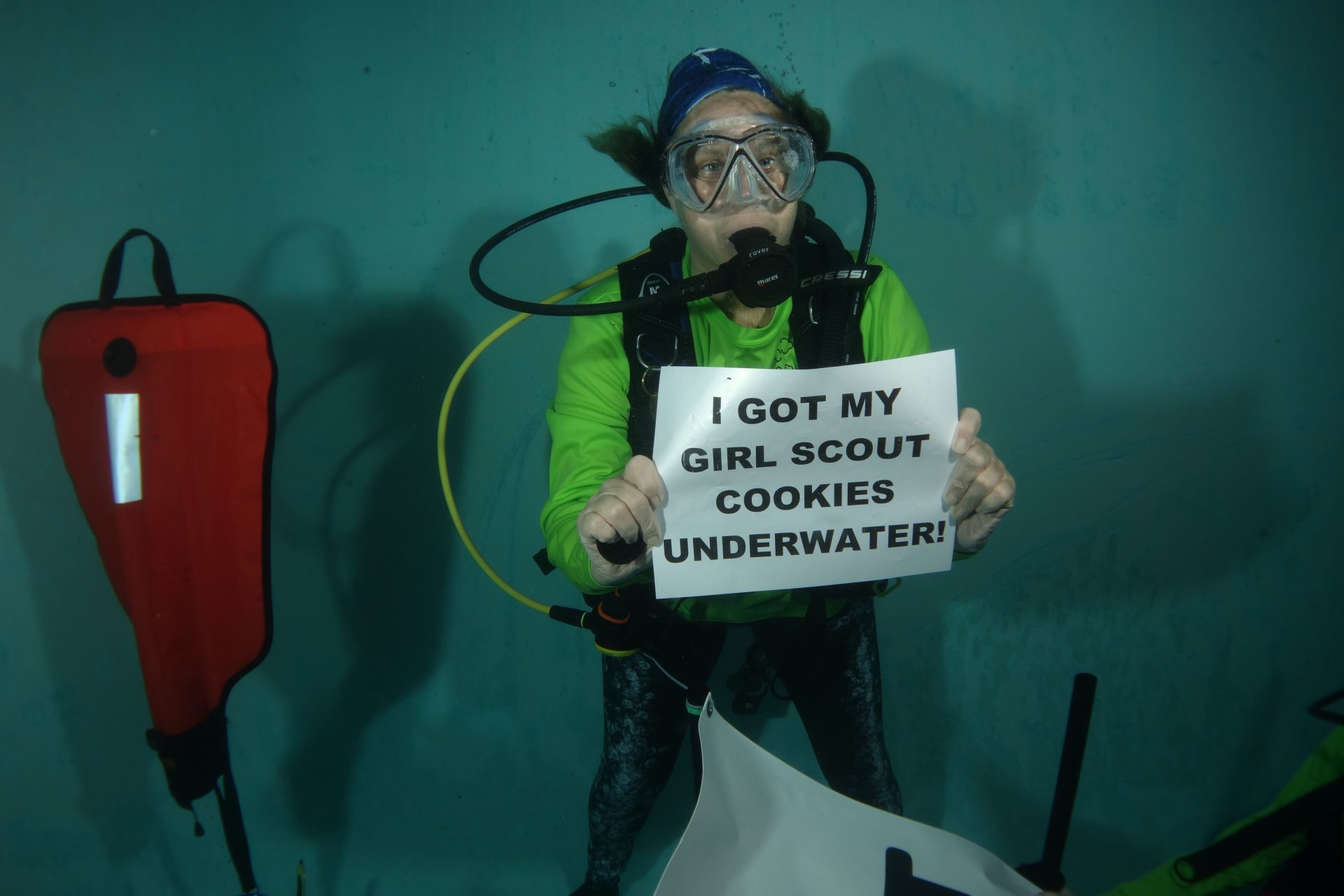 Cookie customer holds up "I got my Girl Scout Cookies underwater!" sign underwater.