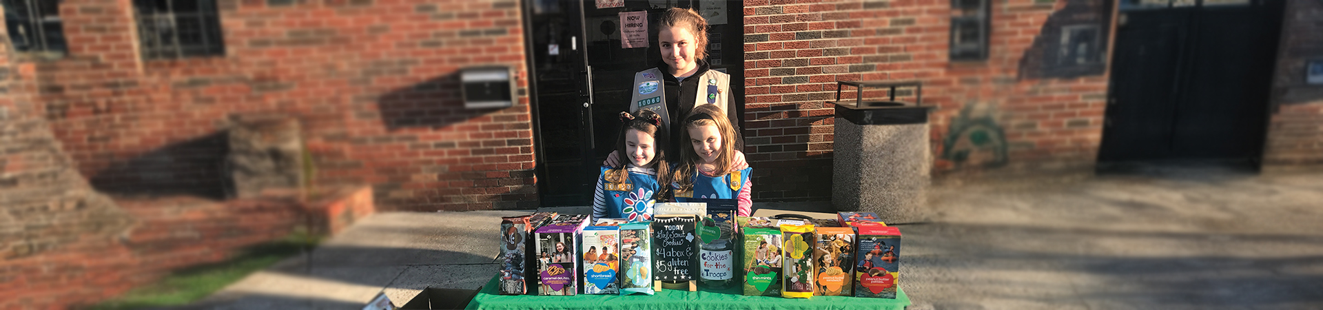 A Cadette Girl Scout posing with two Daisies at a cookie booth 