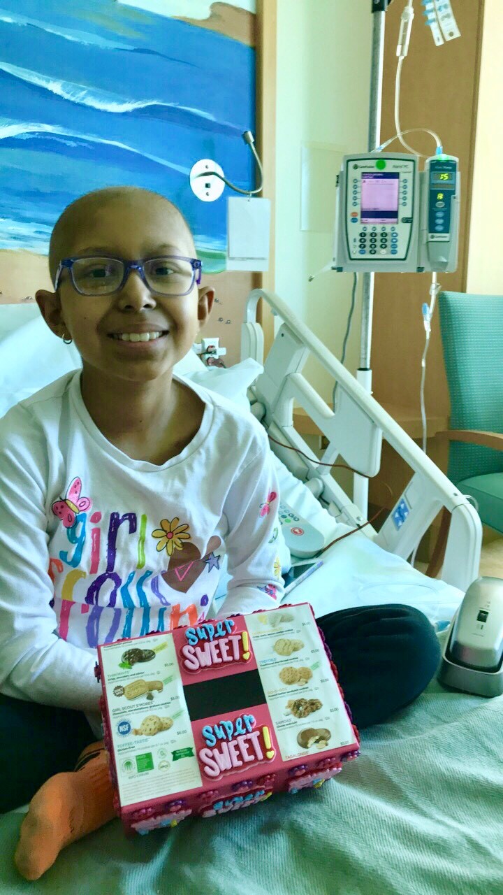 Sarah sitting on her hospital bed with a cookie donation box