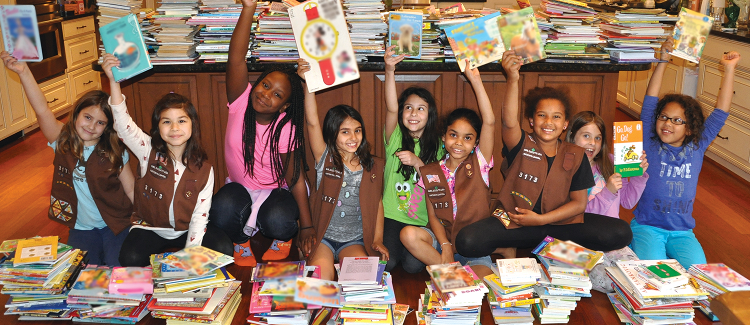 Troop 3173 surrounded by stacks of books, holding books above their heads.