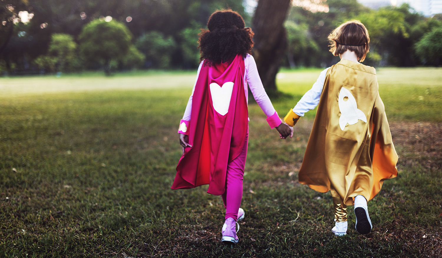  two girls wearing shiny super hero costumes holding hands 