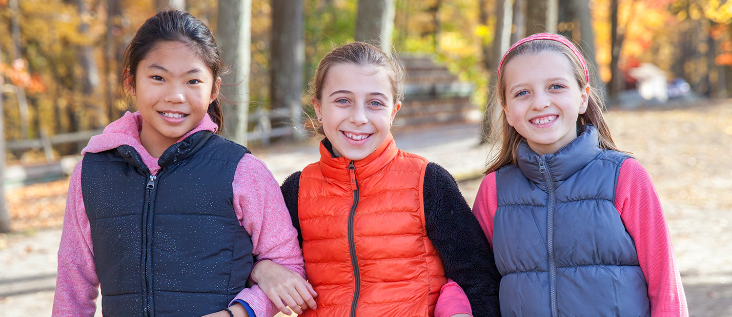  three girls wearing puffy vests with their arms linked 