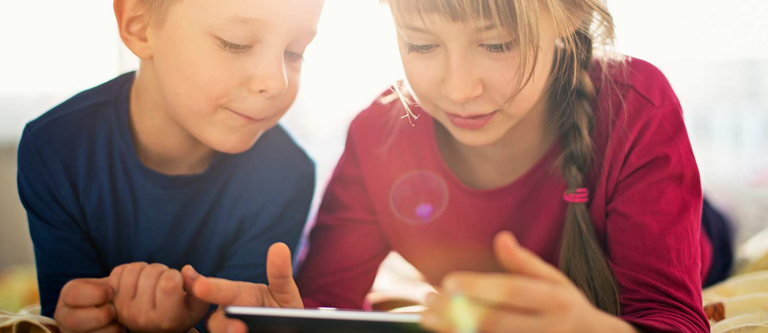  A girl and a boy are reading on a tablet together. 
