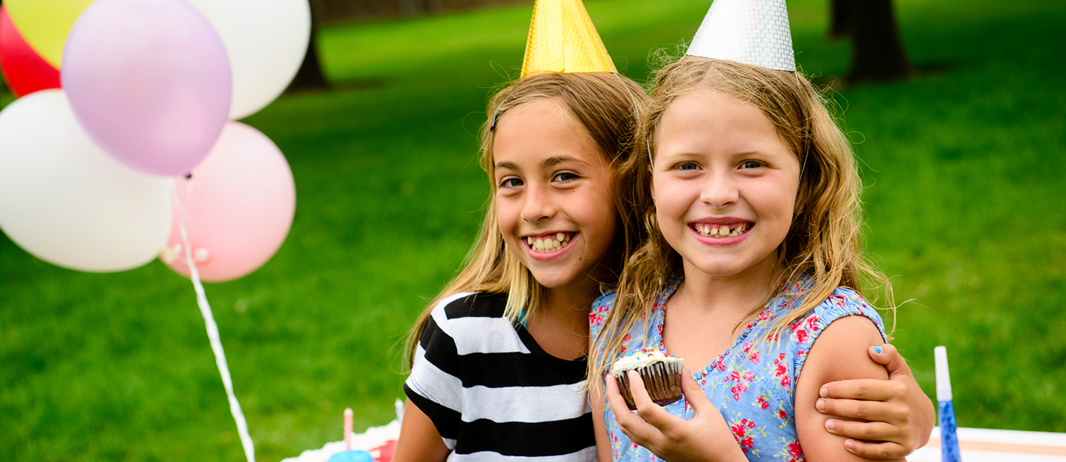  Two happy girls at a birthday party holding cupcakes. 