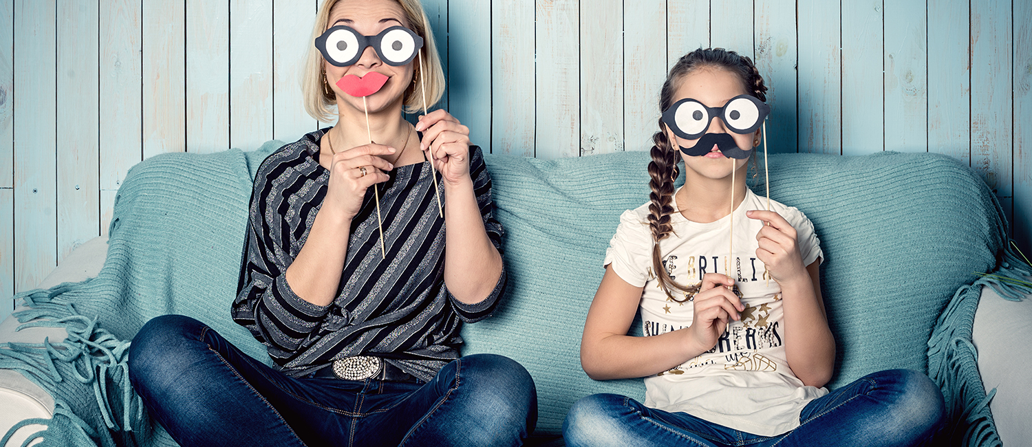  Funny mom and daughter with false mustaches, playing at home. 