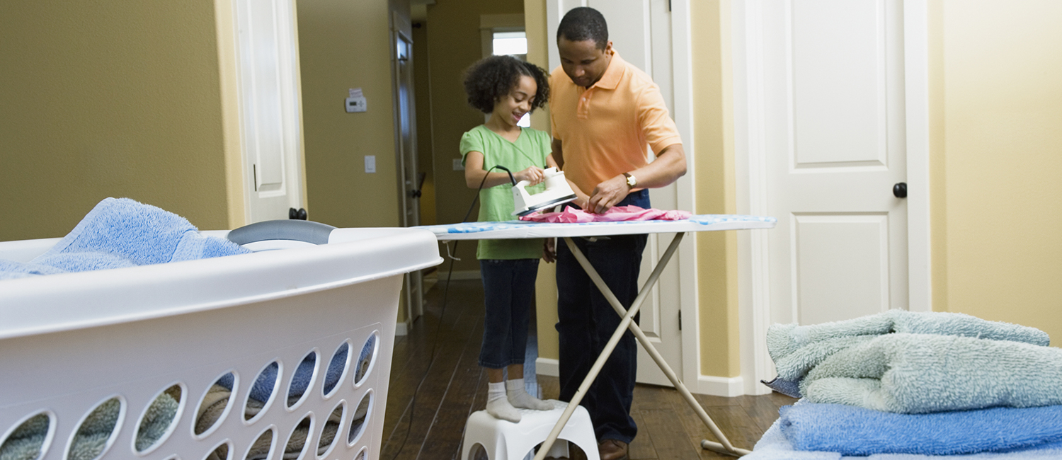  Father next to his young daughter while she learns how to iron. 