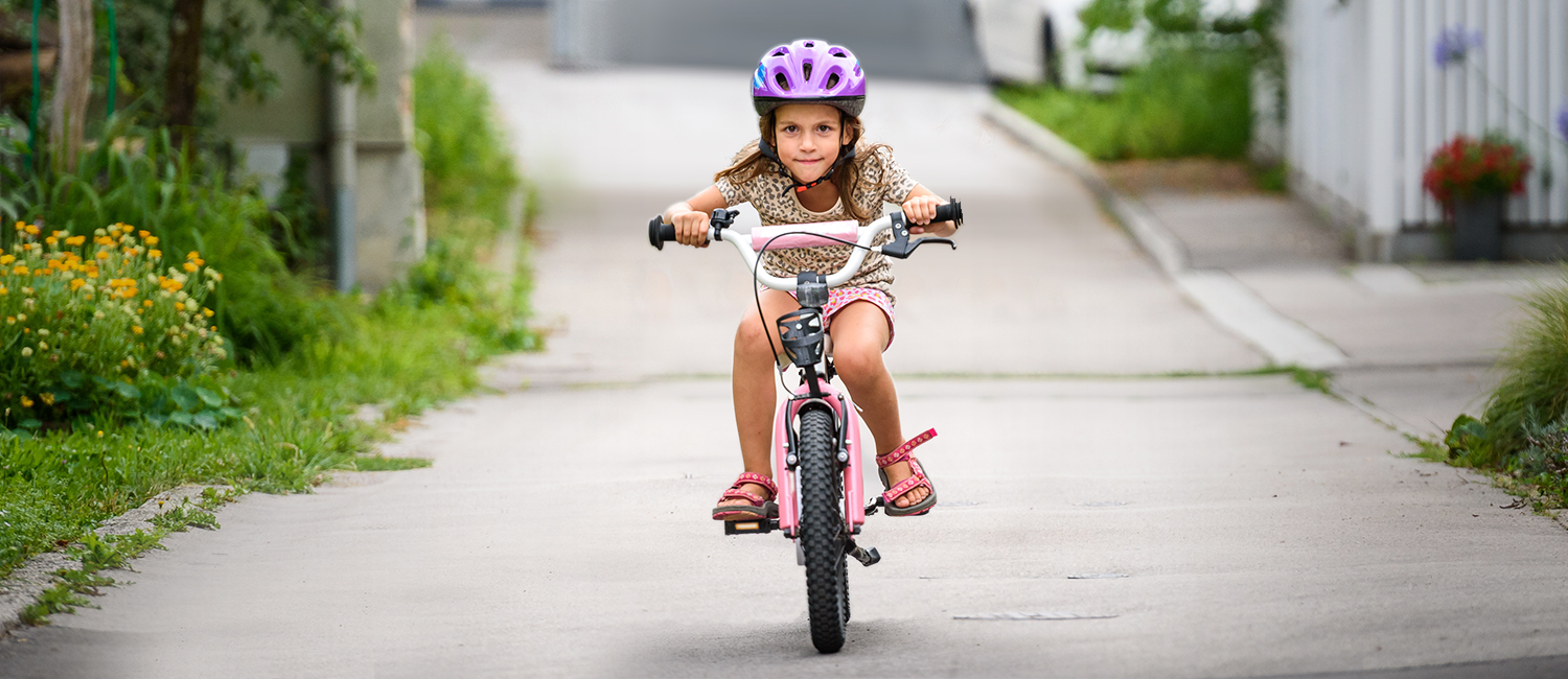  Young girl in a purple helmet riding a bike on the road. 