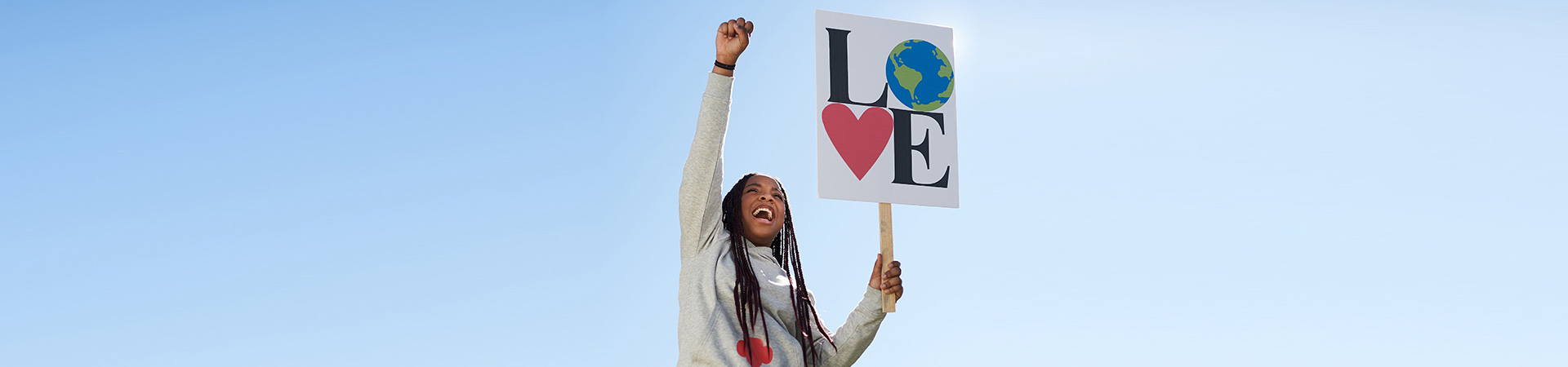  girl holding up a protest sign that says "Love" with an image of the earth for the "o" and a heart for the "v" 