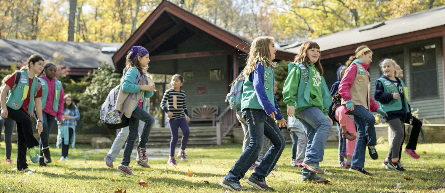  A large group of Girl Scouts walking in front of a large mess hall at a camp 