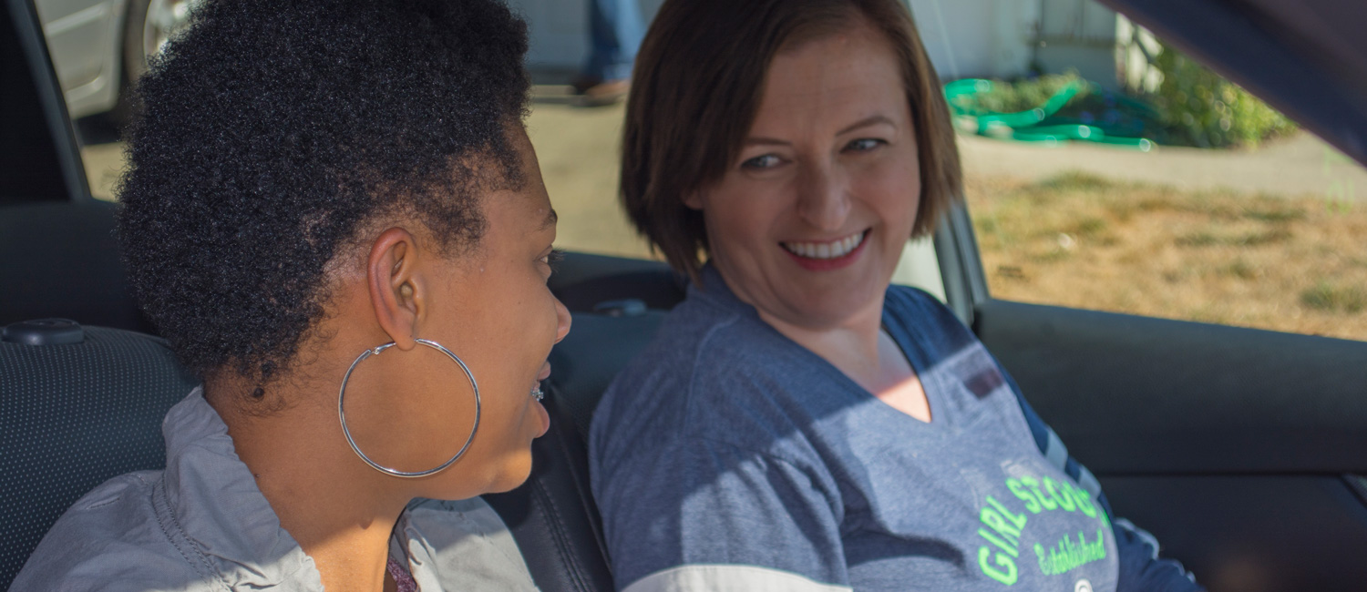  Two volunteers in a car looking at each other and smiling. 