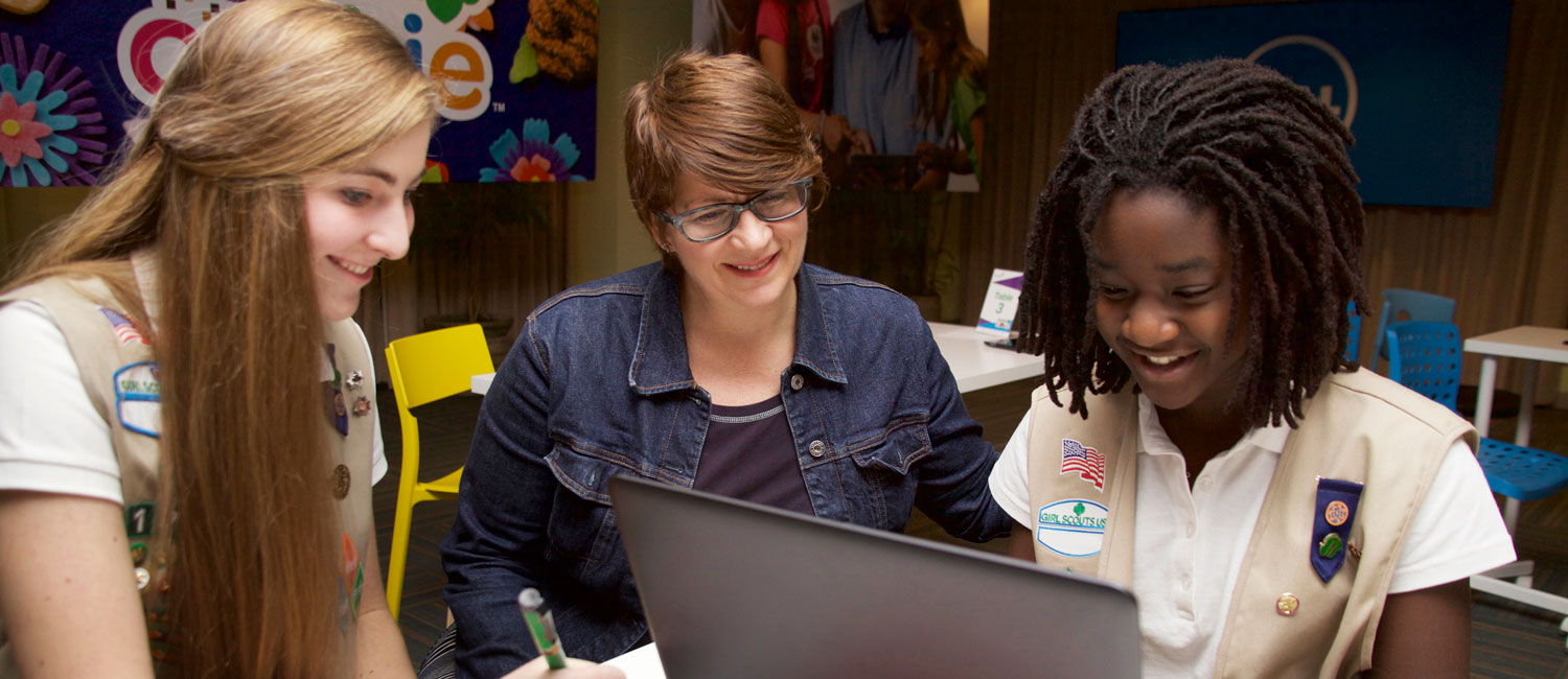  Two Senior Girl Scouts working on a computer with their troop leader.  