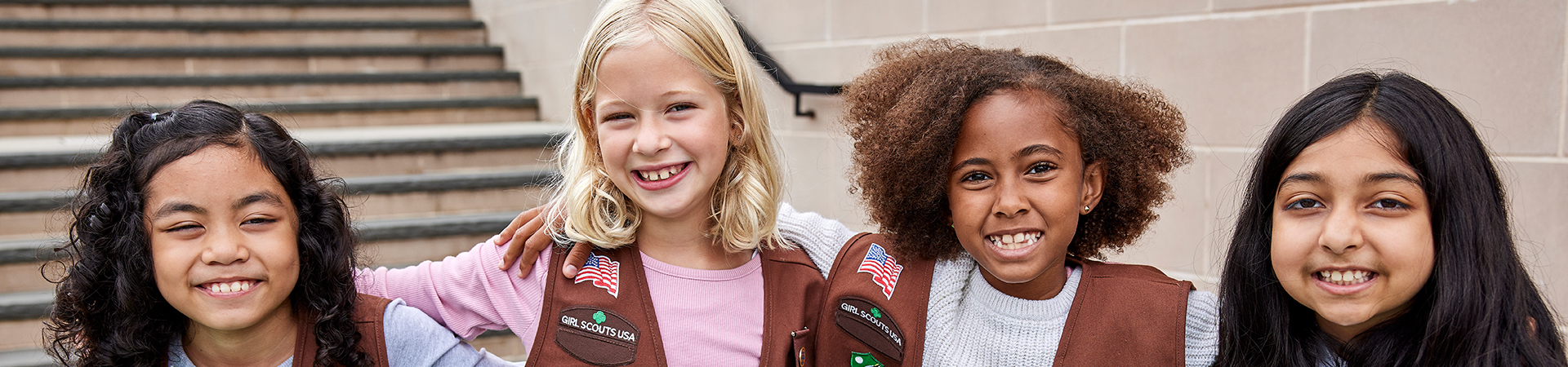  Cuatro Brownie Girl Scouts con los brazos alrededor de los hombros. 