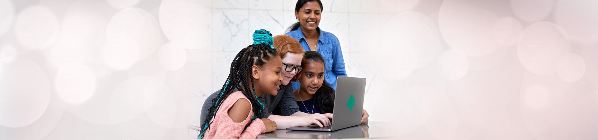  Tres niñas trabajando en una computadora supervisadas por su líder de tropa 